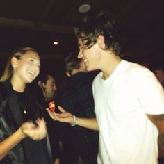 two young men laughing while standing next to each other in front of people at a party