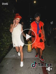 two people dressed in costumes walking down the street at night with one person talking on a cell phone