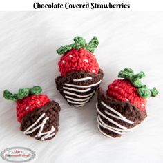 three crocheted strawberries are sitting on a white furnishing area, one is brown and the other is red