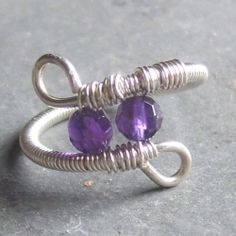 two silver rings with amethyst purple glass beads on each end, sitting on a gray surface