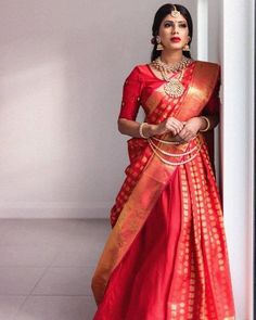 a woman in a red and gold sari standing next to a wall with her hands on her hips