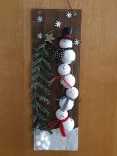 a snowman hanging on the side of a wooden door with ornaments around it and evergreen branches