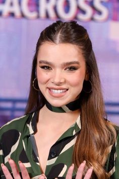 a woman with long hair wearing a green shirt and gold hoop earrings smiles at the camera