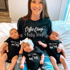 a woman sitting on top of a bed with three baby dolls in her lap and wearing matching shirts