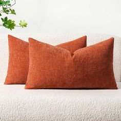 two orange pillows sitting on top of a white couch next to a potted plant