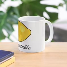 a white coffee mug with a yellow lemon on it sitting on a table next to a book