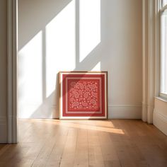 a red framed artwork sitting on top of a hard wood floor next to a window