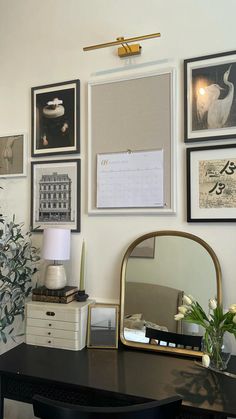 a desk with a mirror, lamp and pictures on the wall