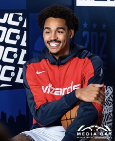 a smiling man sitting in front of a wall with basketballs on it's sides