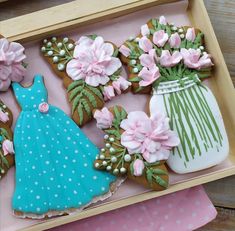 some decorated cookies in a box with flowers and vases on the table next to them