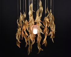 a chandelier made out of gold leaves hanging from it's sides with a light bulb in the middle