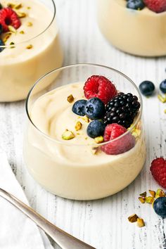 two desserts with berries, blueberries and pistachio in them on a white table