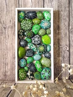 a white box filled with lots of green and white painted rocks on top of a wooden table