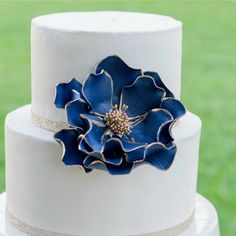 a three tiered white cake with blue flowers on the top and gold trimmings