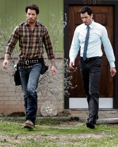 two men walking in front of a house with one wearing a tie and the other carrying a bag