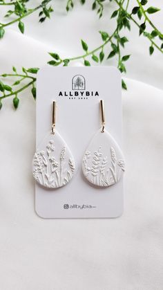 a pair of white earrings sitting on top of a card next to some flowers and leaves