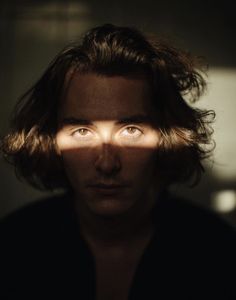 a man with long hair and blue eyes looking at the camera while he's shadow is cast on his face