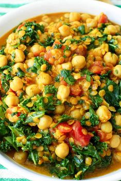 a white bowl filled with chickpeas, spinach and tomato soup on top of a green table cloth