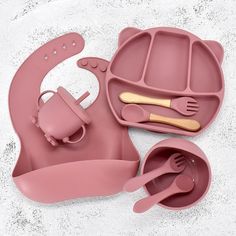 a pink baby feeding set with utensils and spoons on a white surface