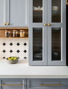 a bowl of fruit sitting on top of a kitchen counter next to cabinets with glass doors