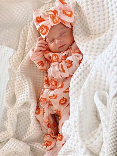 a baby wrapped up in a blanket and wearing an orange pumpkin print headband with the letter s on it