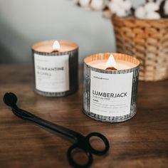 two candles sitting on top of a wooden table next to a pair of scissor