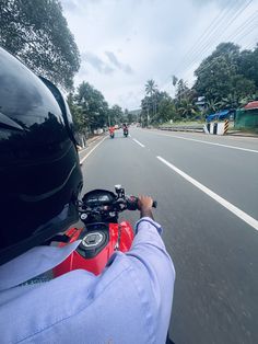 a person riding a motorcycle down a street next to a lush green forest on a cloudy day