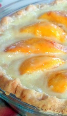 a close up of a pie with peaches on top in a glass dish sitting on a table