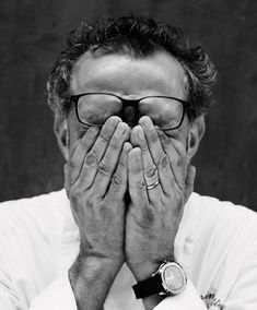 a black and white photo of a man covering his face with both hands while looking at the camera