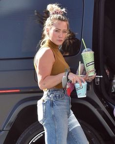 a woman is stepping out of a bus and holding a drink