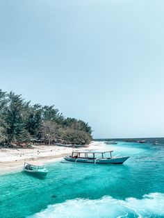 two boats are sitting on the beach in clear water