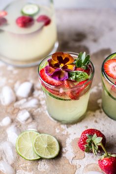 two glasses filled with fruit and ice on top of a table next to sliced strawberries