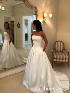 a woman standing in front of a mirror wearing a white wedding dress and looking at herself in the mirror