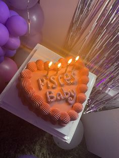 a heart shaped birthday cake with candles on it in front of purple and white balloons