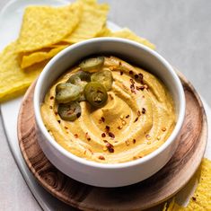 a white bowl filled with hummus and pickles next to tortilla chips