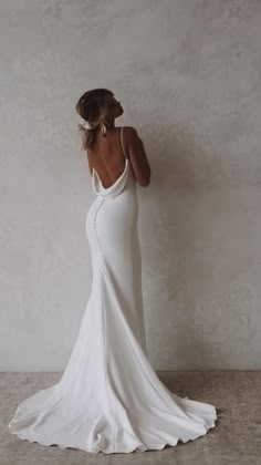 a woman in a white wedding dress is standing against a wall with her back to the camera