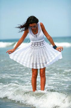 a woman standing on top of a wave in the ocean while wearing a white dress