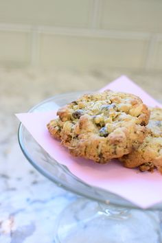 two cookies sitting on top of a pink napkin next to a glass bowl filled with chocolate chips