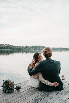 a bride and groom sitting on a dock by the water