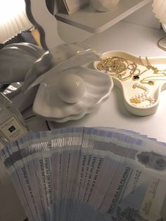 a stack of money sitting on top of a counter next to a plate with gold jewelry