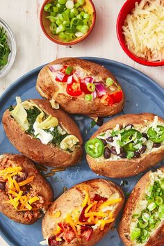 several baked potatoes on a blue plate topped with cheese and veggie toppings