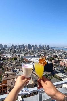 two people toasting with drinks in front of a cityscape and the ocean