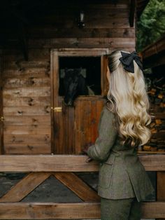 a woman with long blonde hair wearing a green suit and black bow sitting on a wooden bench