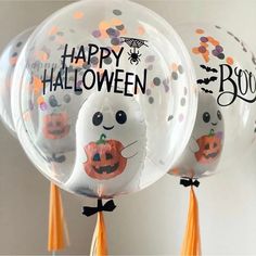 three clear balloons with happy halloween designs on them, hanging from orange tassels