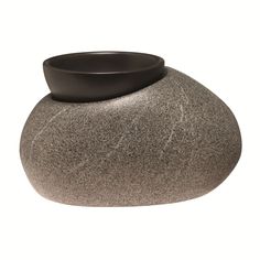 a black bowl sitting on top of a gray stone vase with a white base in front of it