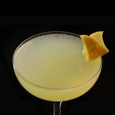 a close up of a drink in a glass with an orange peel on the rim