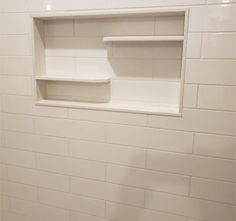 an empty white shelf in the middle of a tiled wall with no one around it