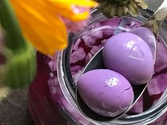 three purple eggs are in a jar with spoons and flowers on the table next to it