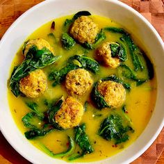 a white bowl filled with meatballs and spinach on top of a wooden table