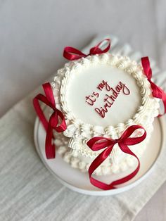 a white cake with red ribbon around it on top of a table next to a napkin